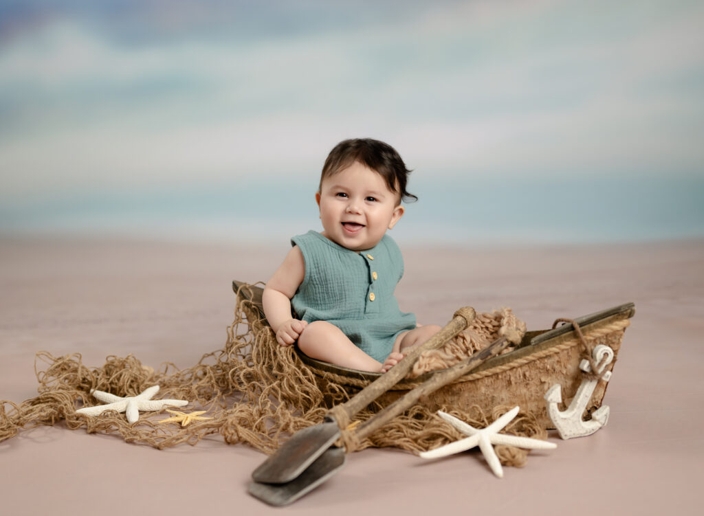 Baby sitting up in a tiny wooden boat and smiling.