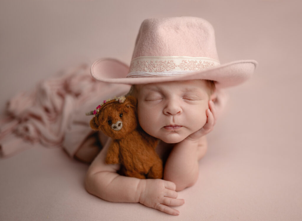 Newborn baby sleeping with cowgirl hat and felted highland cow.
