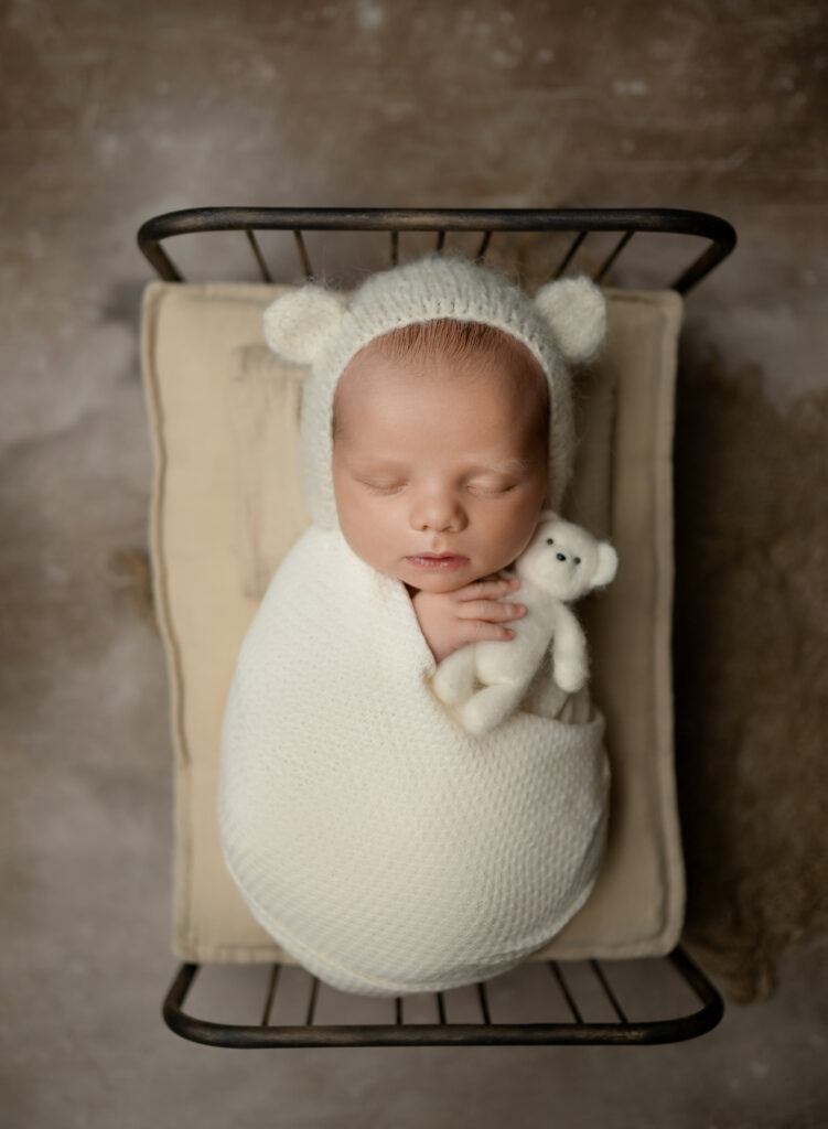 Baby sleeping in newborn bed with teddy bear.