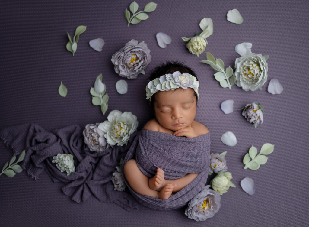 Baby girl swaddled and sleeping with loose florals around her.