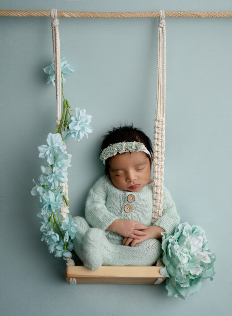 newborn baby girl in mint romper, sleeping on a swing.