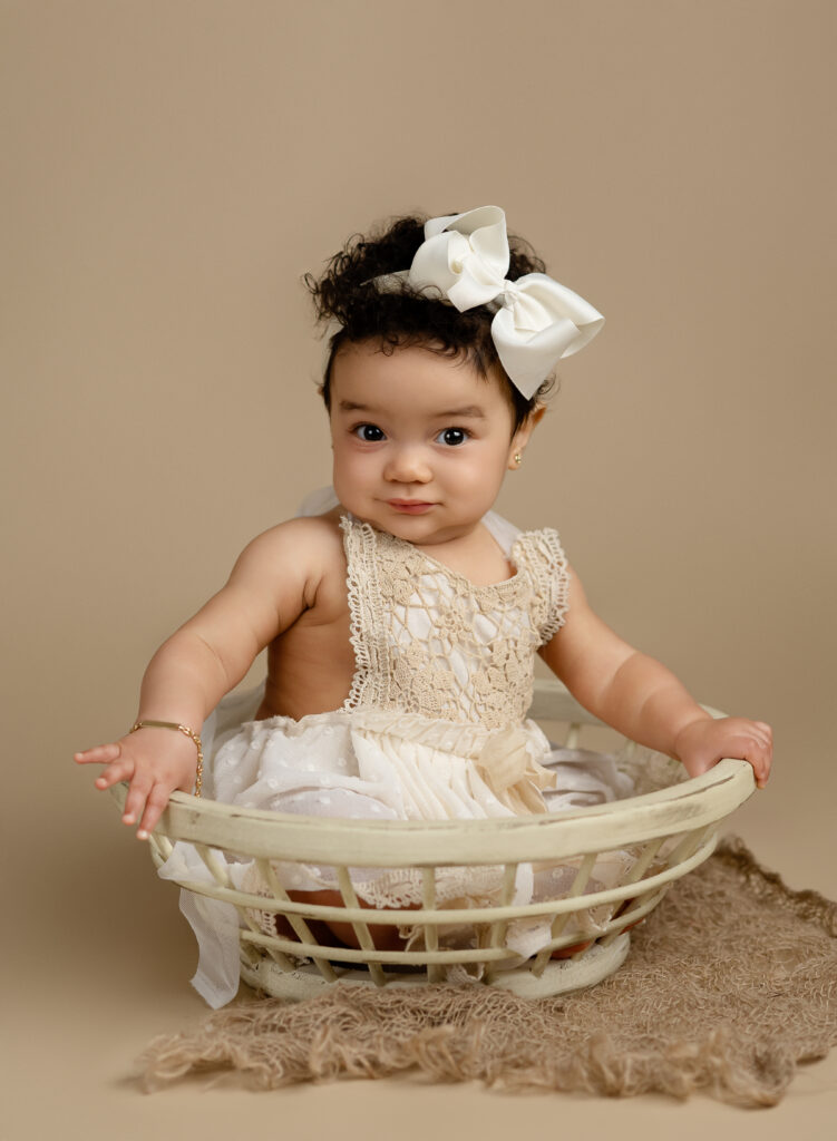 Baby girl sitting up in a wooden cream bowl.