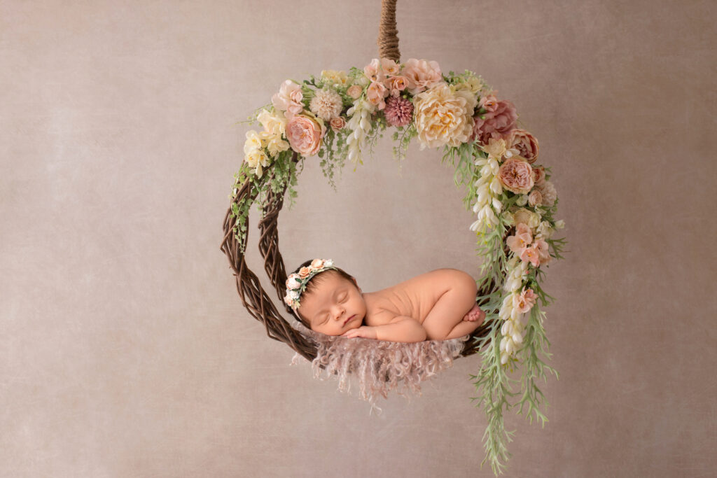 Naked baby sleeping on floral swing.