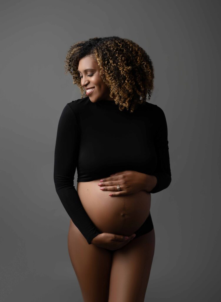 Women in black crop top and black underwear holding her baby bump and smiling. Photographed at Atlanta Maternity Photo Studio