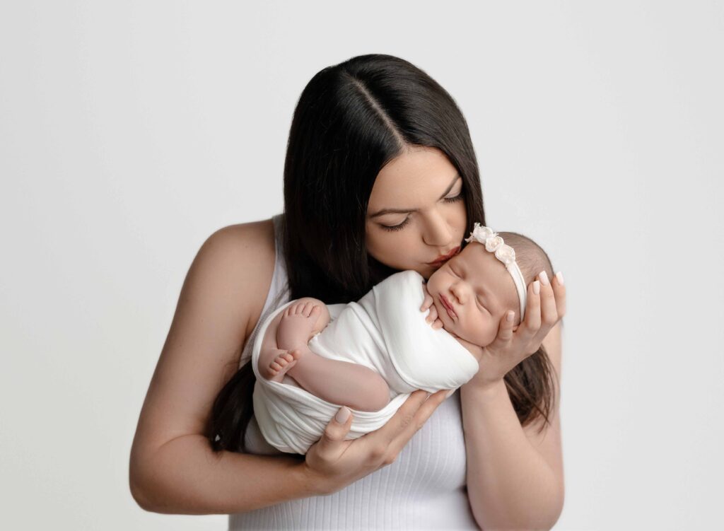 Women with dark hair kissing baby girl swaddled in a white wrap.