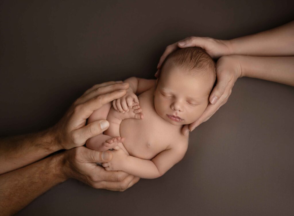Naked baby sleeping with Mom cradling his head and dad cradling his feet.