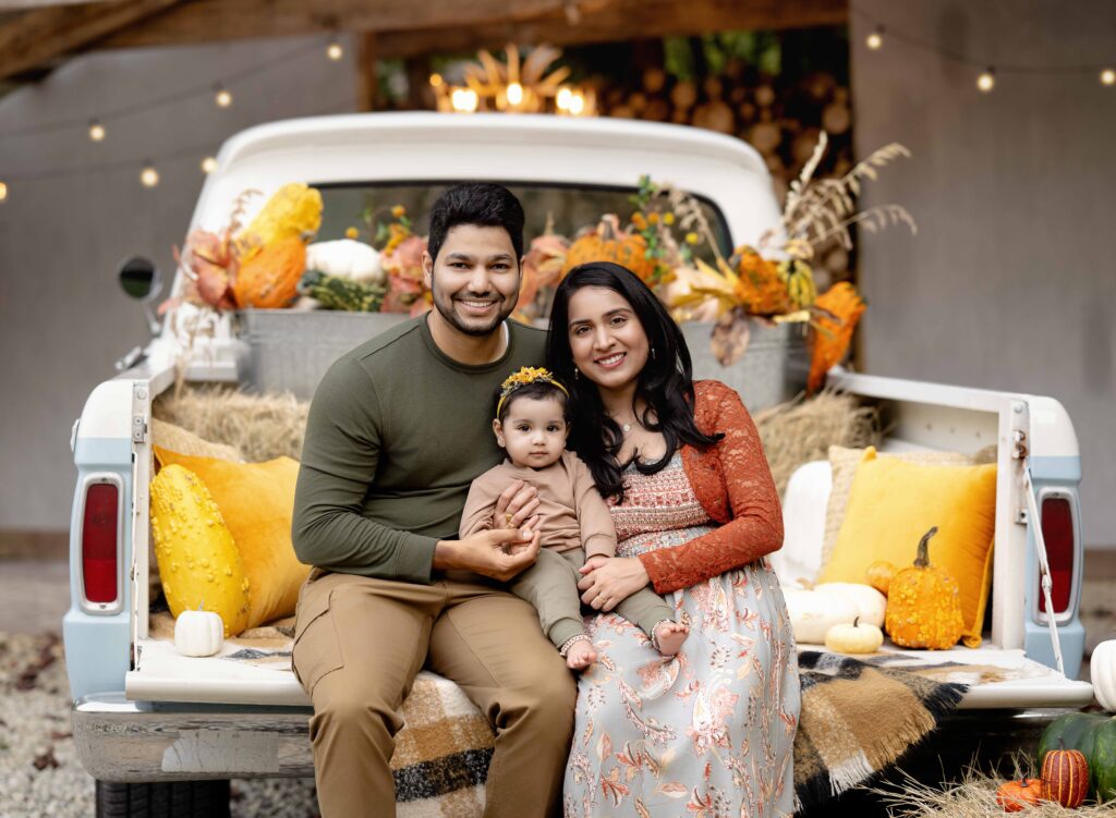 Vintage truck with fall decor and family of 3 sitting on the tailgate.