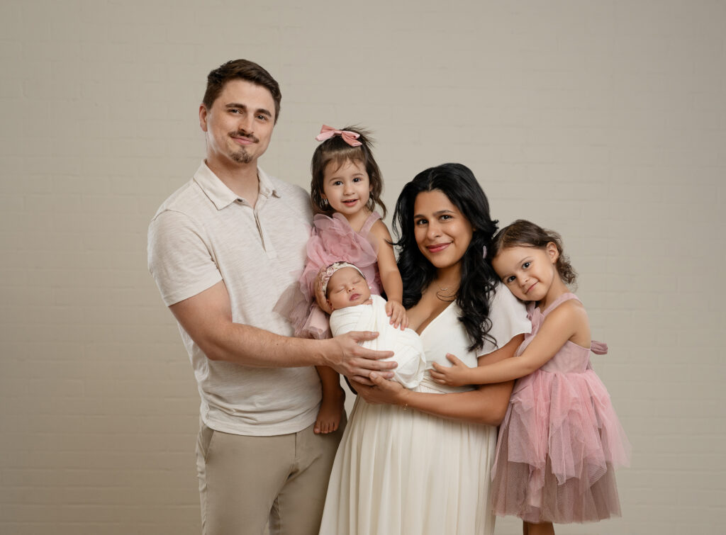 Family of 5 with a newborn girl and two older sisters in pink dresses, taking a family portrait at Atlanta family photo studio.