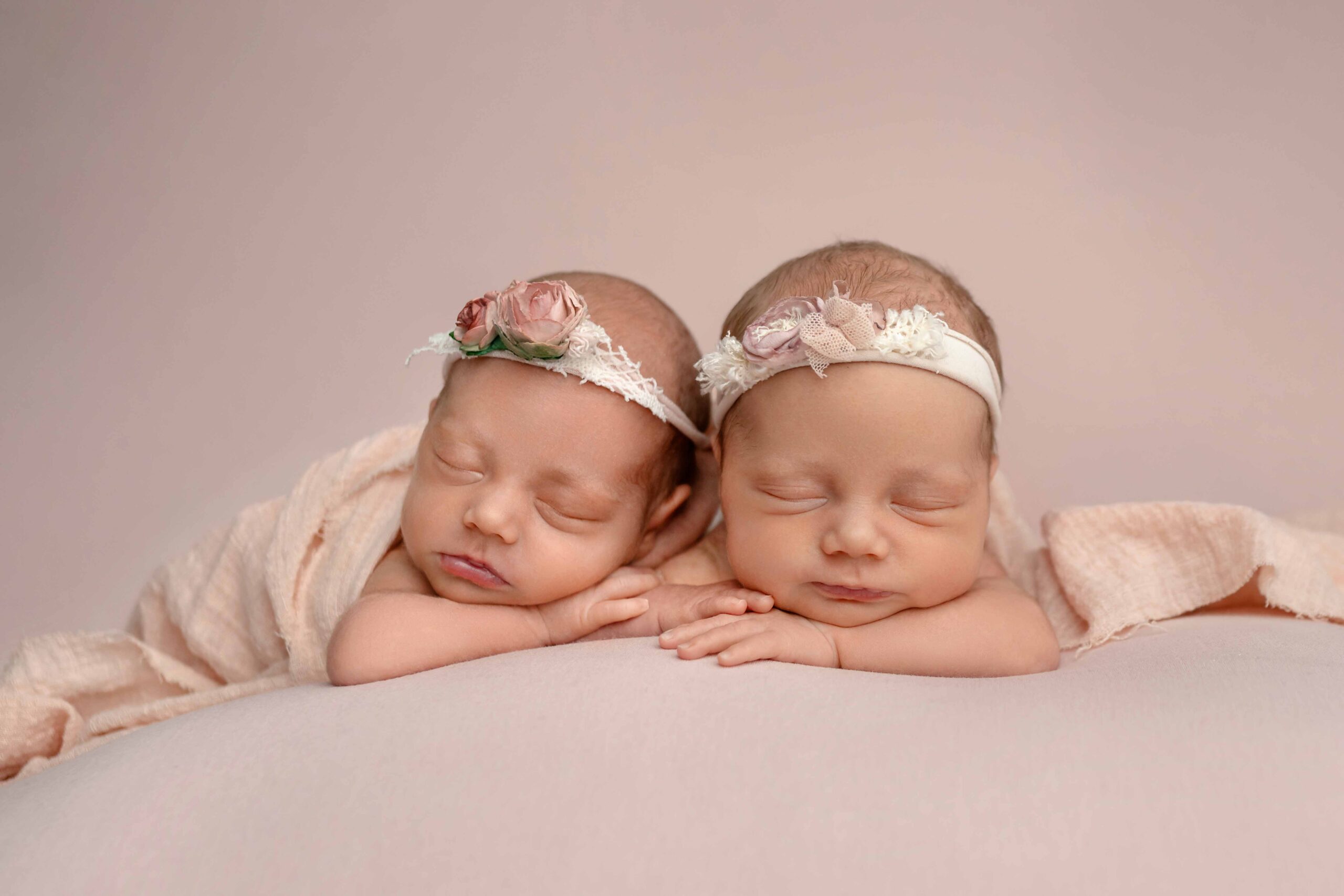Close up photo of twin baby girls laying on their hands, sleeping.