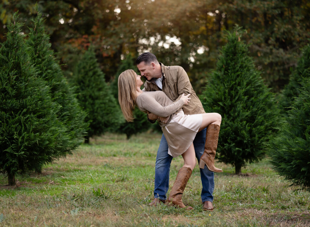 Dad dipping Mom back and leaning in nose to nose on a tree farm for their Christmas photoshoot.