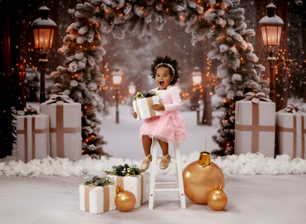 Little girl in pink dress holding a present with a surprise face on a winter wonderland backdrop set in Atlanta.