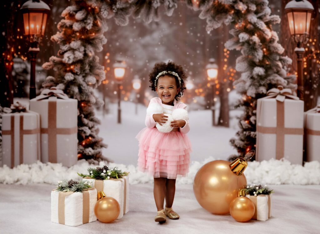 Little girl holding snowballs on a winter wonderland backdrop set taking holiday photos at Atlanta photography studio.