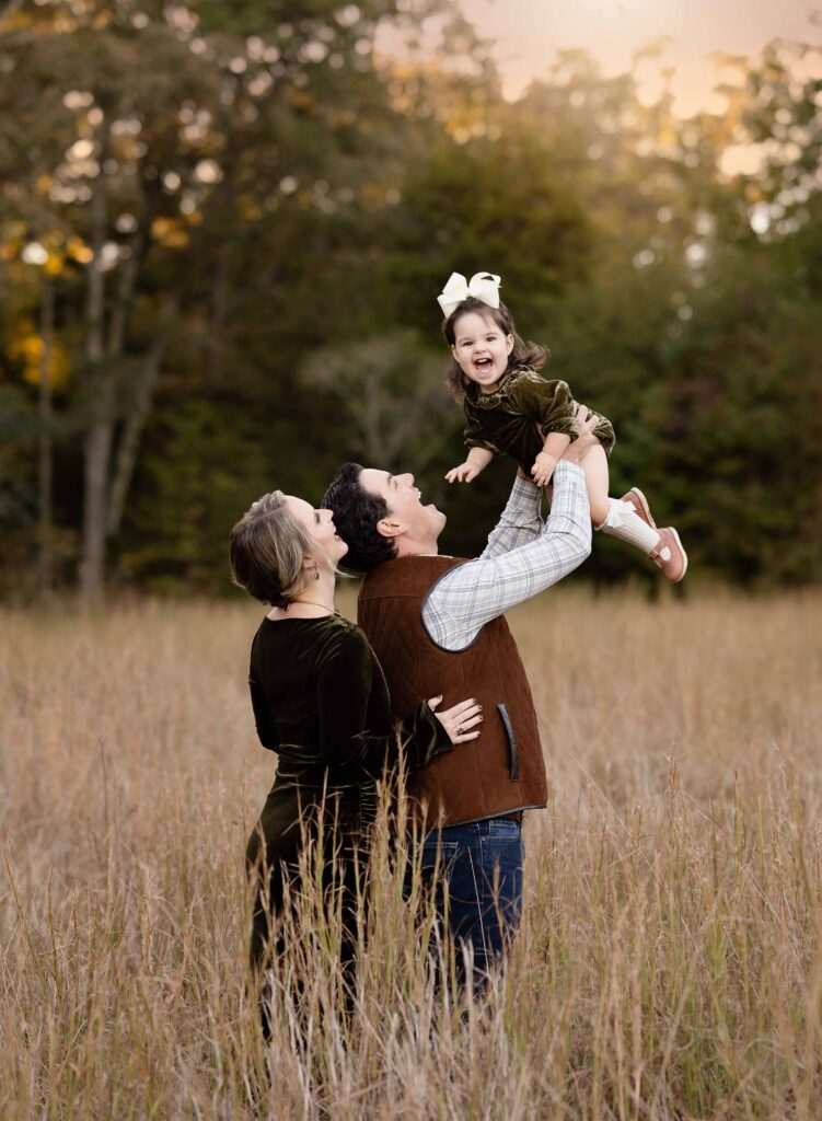 Family playing in hay field and tossing child in air.