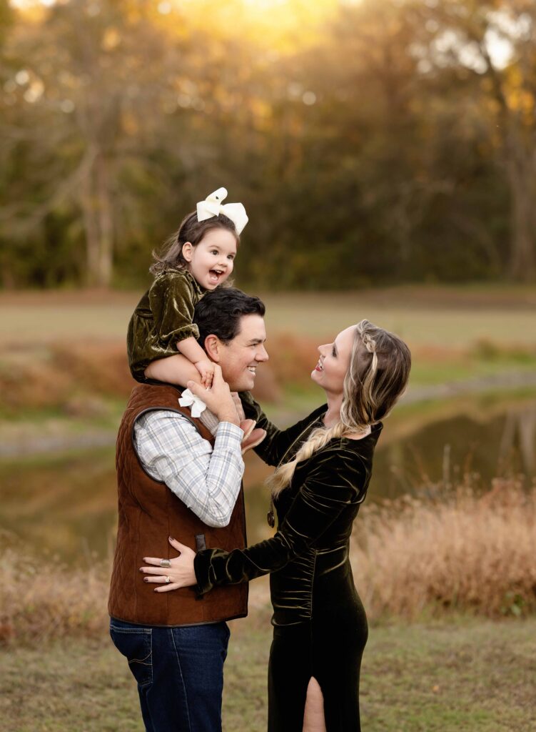 Toddler on dad's shoulders and mom leaning in smiling.