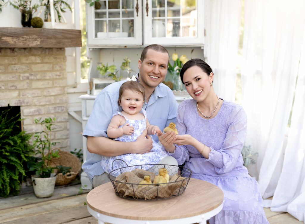 Family of 3 taking easter photos with baby chicks in a white greenhouse.