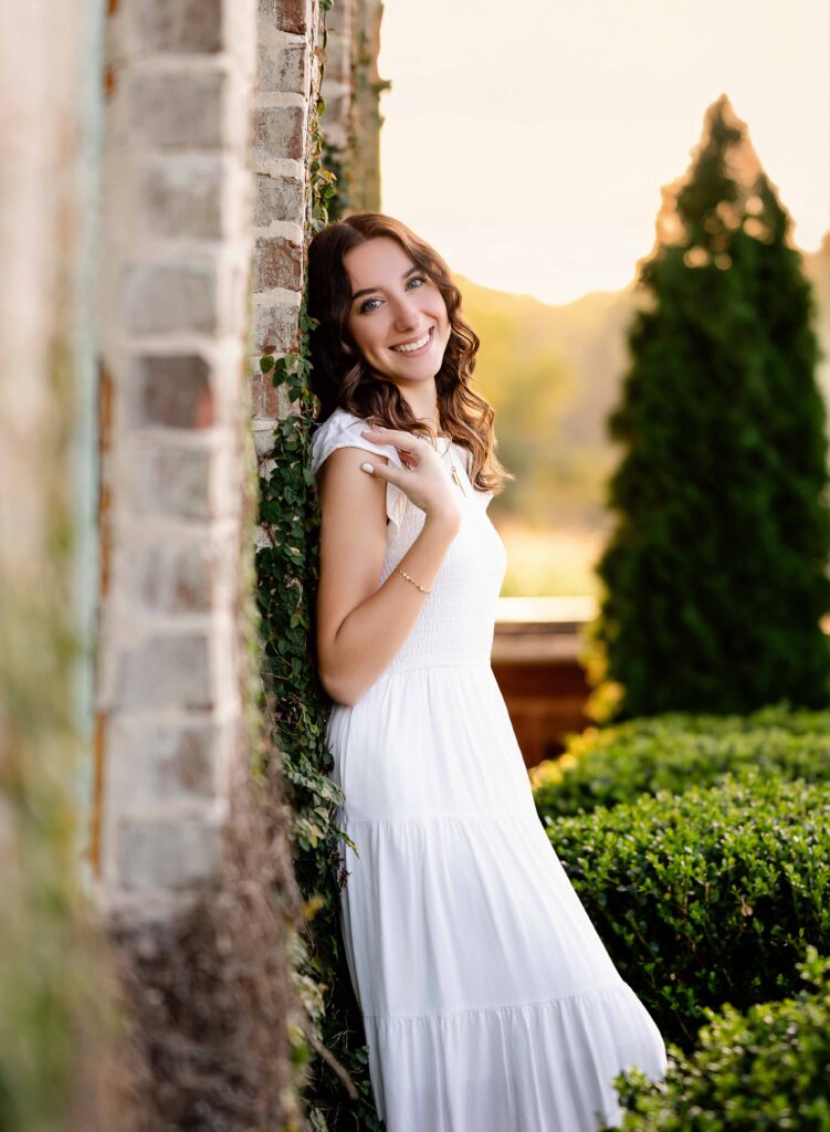 Grad leaning against a brick wall, taking senior photos.