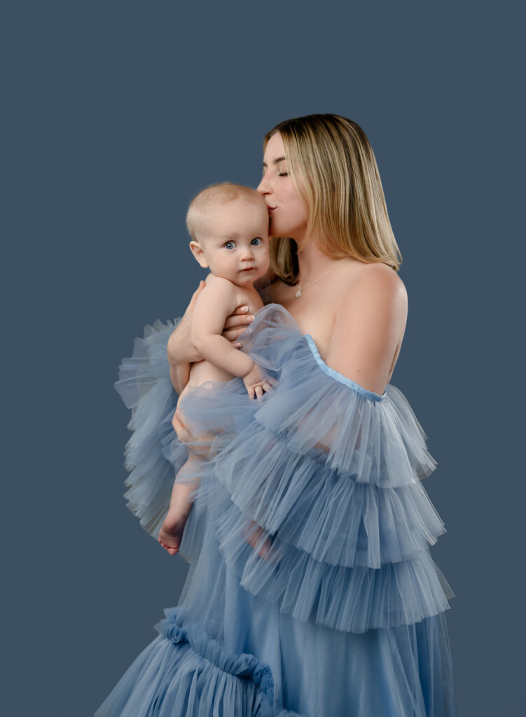 Mommy and me photo of Mom in blue gown snuggling naked baby.