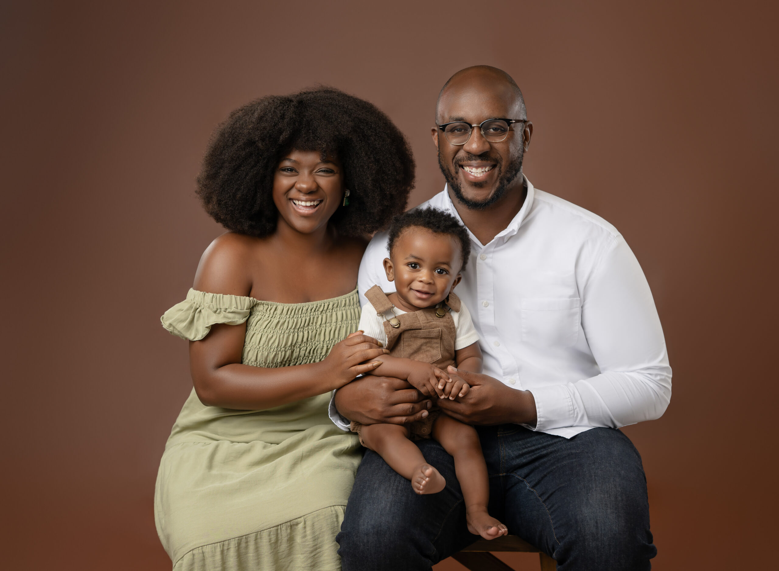 Mom, dad and baby boy taking photos on a chestnut backdrop.