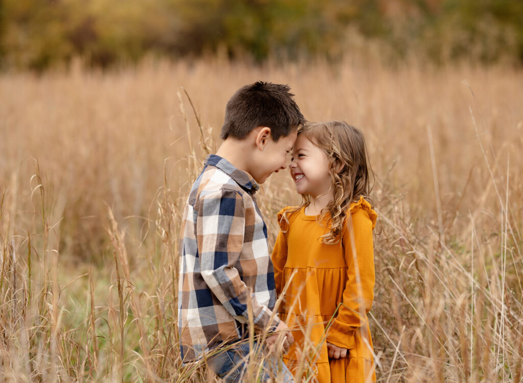 Brother and sister touching noes and giggling.
