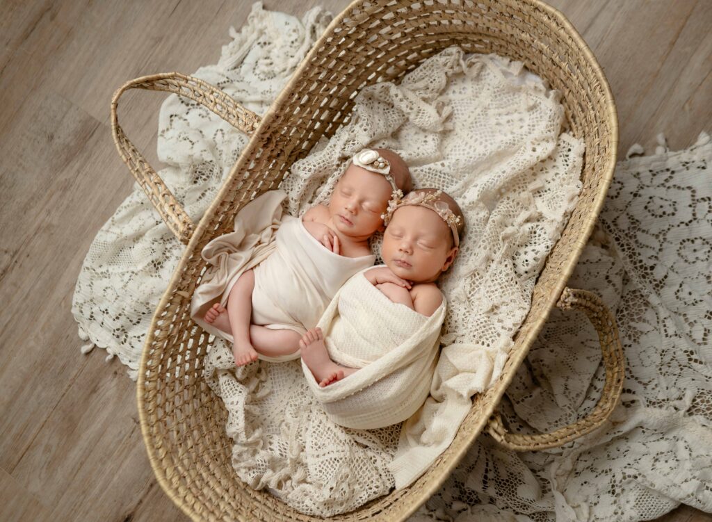 Twin newborn girls swaddled and sleeping in a moses basket.