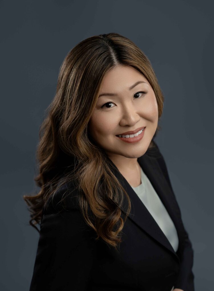 Headshot of women in navy suit jacket on a blue background and smiling.