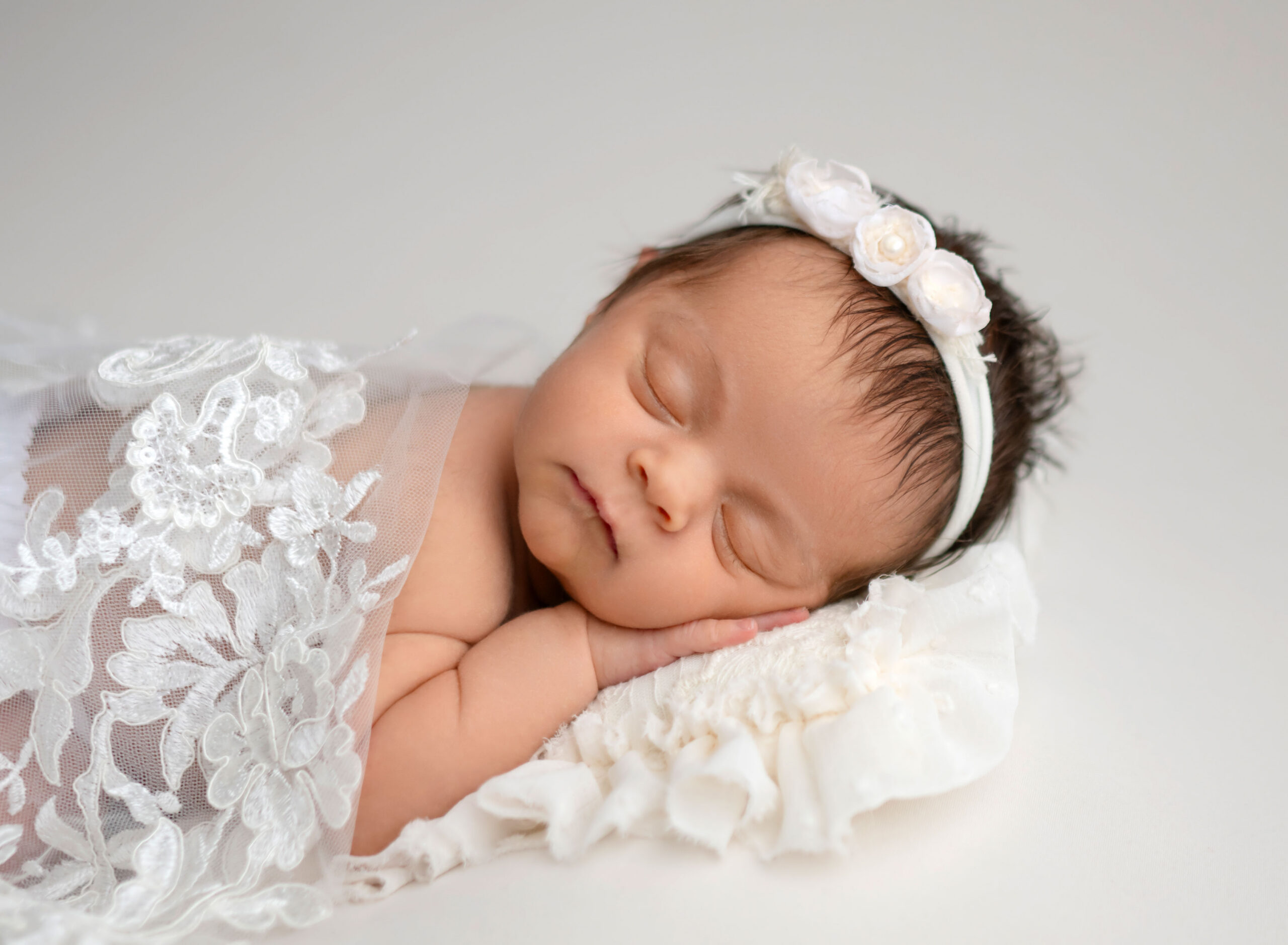 Newborn baby girl sleeping on pillow with lace fabric over her back.