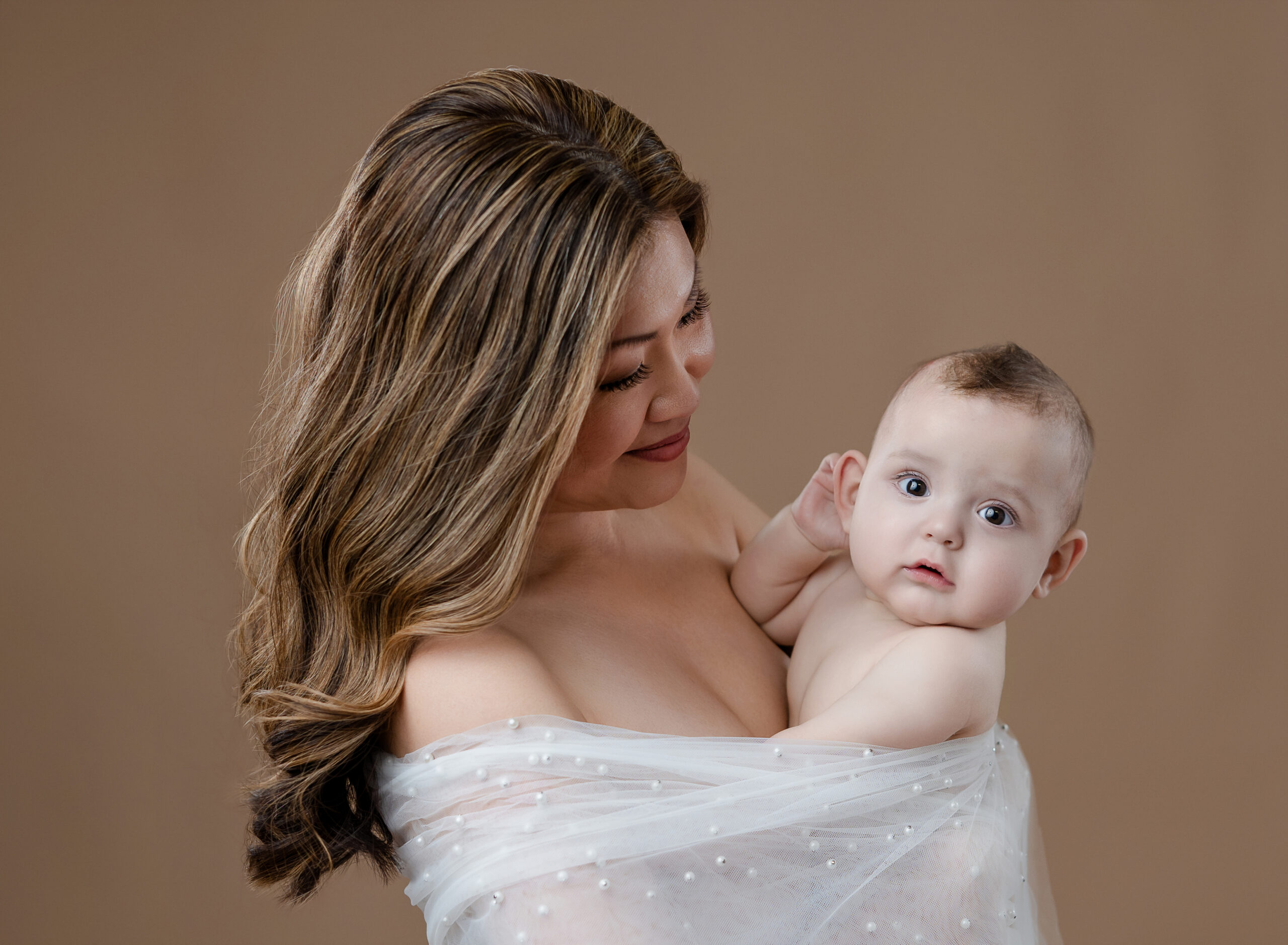 Mom and baby boy wrapped in white pearl drape for an intimate motherhood portrait.